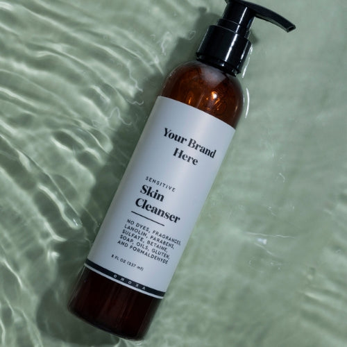 Brown bottle of sensitive skin cleanser with a pump on a greenish water background